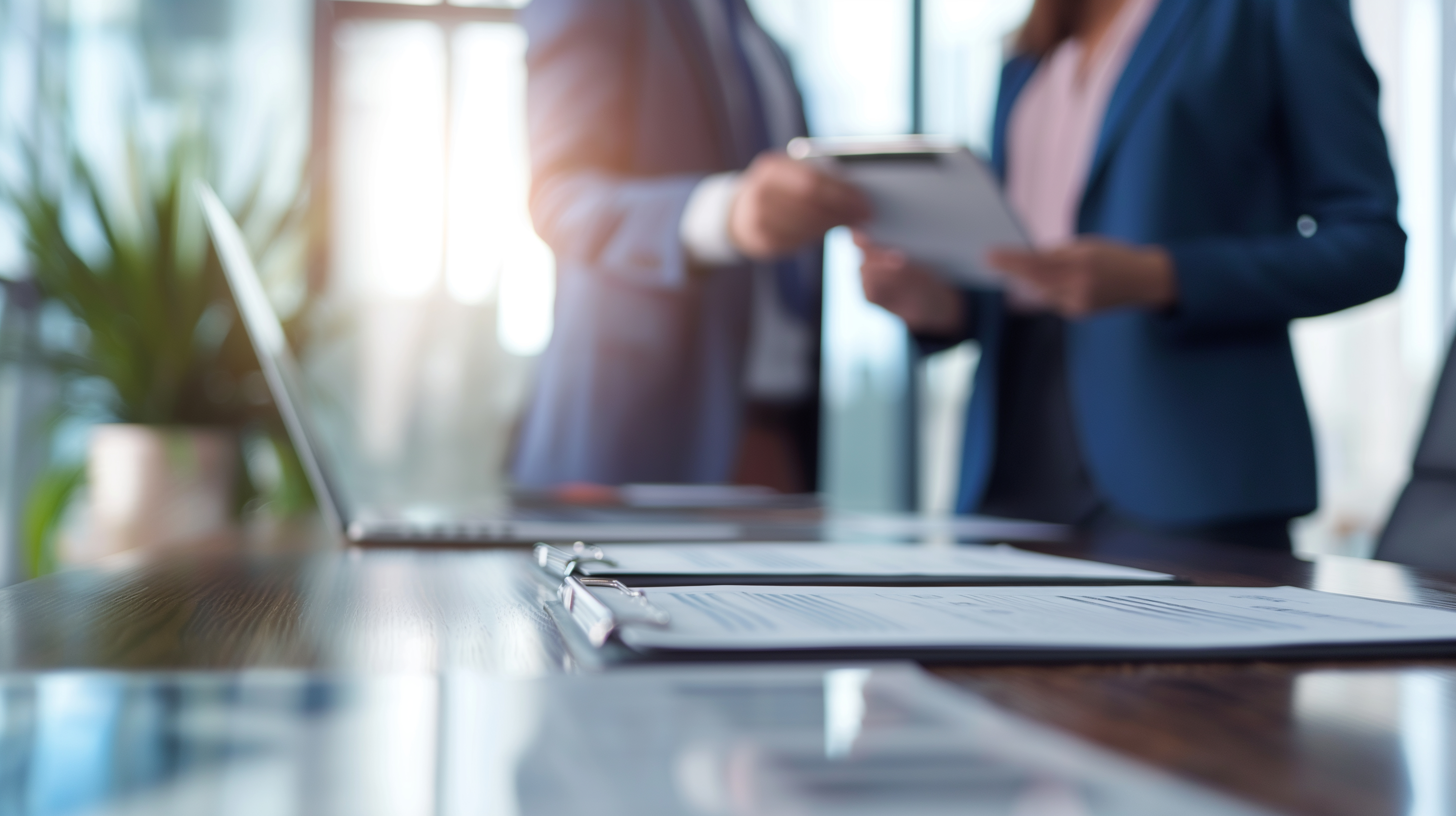 A strategic alliance discussion in a minimalist boardroom, where a businessman and a businesswoman layout partnership terms with digital contracts