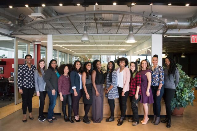 thirteen racially diverse women lined up in an office at a tech conference